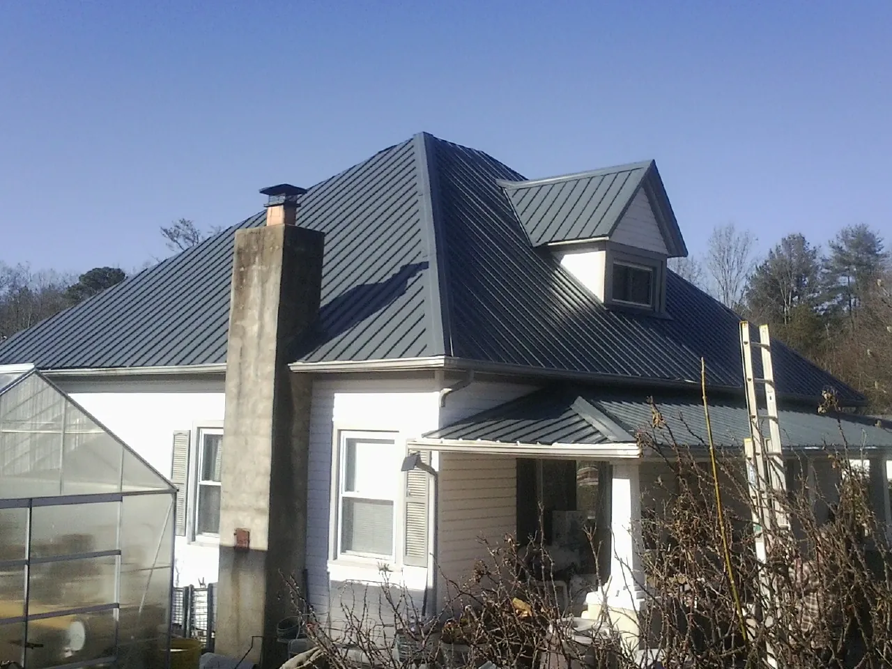 Dark blue standing seam metal roof on a white farmhouse with dormer — Slate & Tile Roof Repair by Roofing Brothers in North Vernon