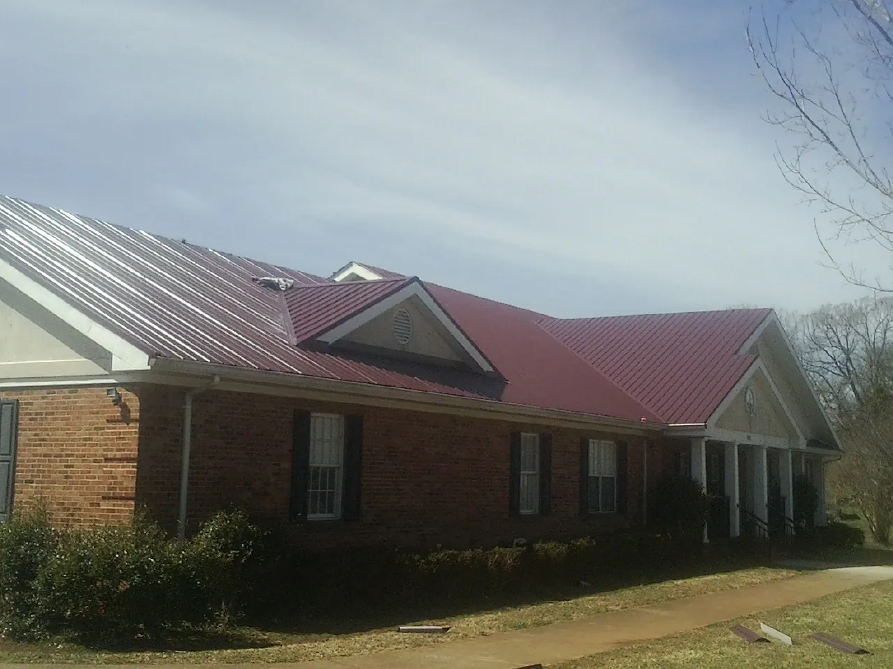 Red metal roof with gabled entries on a long brick building, from a Hail Damage Roof Repair job in North Vernon