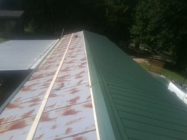 Old rusted panels beside newly installed green metal roofing — Wind Damage Roof Repair by Roofing Brothers in North Vernon