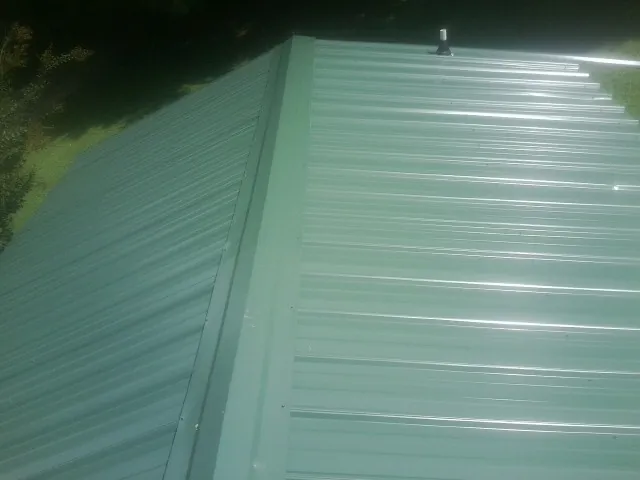 New green metal panels meeting at the ridge of a roof — Flat Roof Repair work by our crew in North Vernon