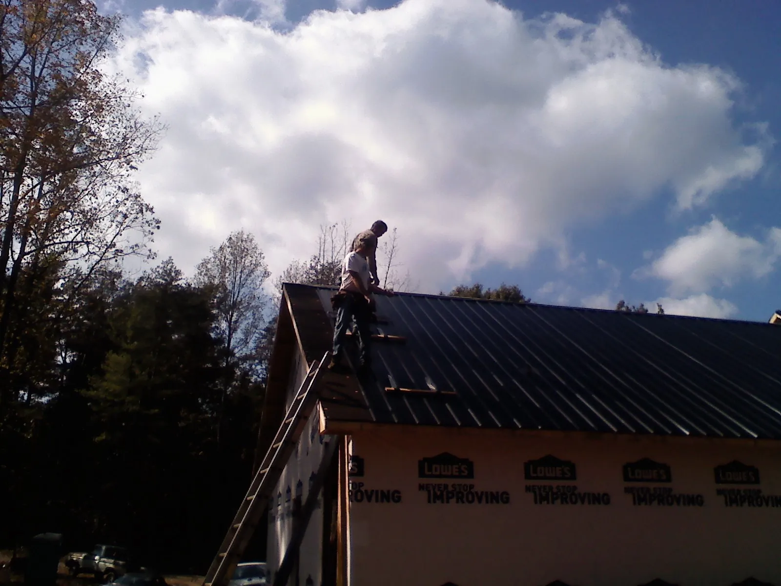 Roofer fastening dark metal panels high against a cloudy sky, from a Roof Inspection job in North Vernon