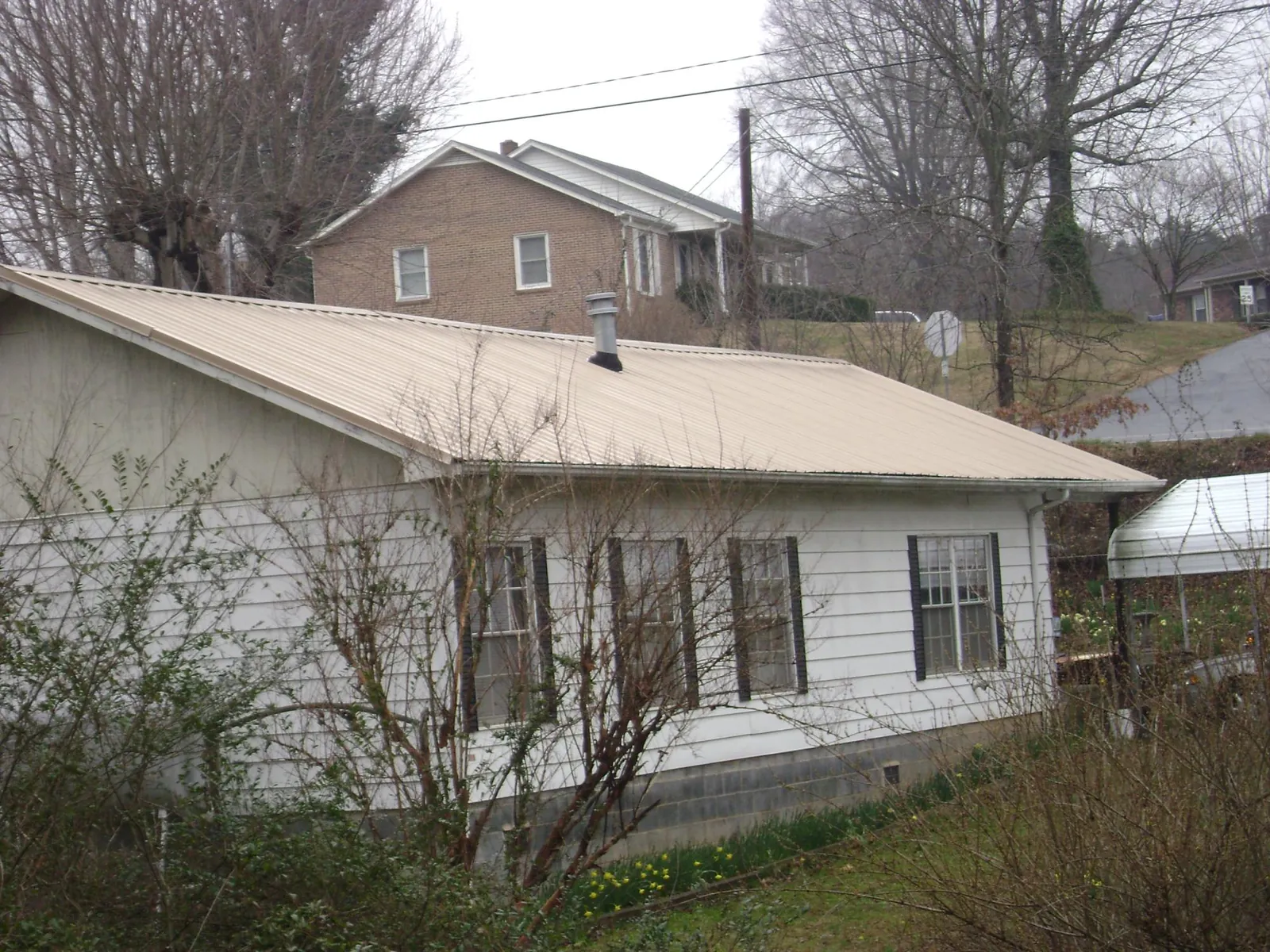 Tan metal roof on a white sided house set into a hillside — Commercial Roofing by Roofing Brothers in North Vernon