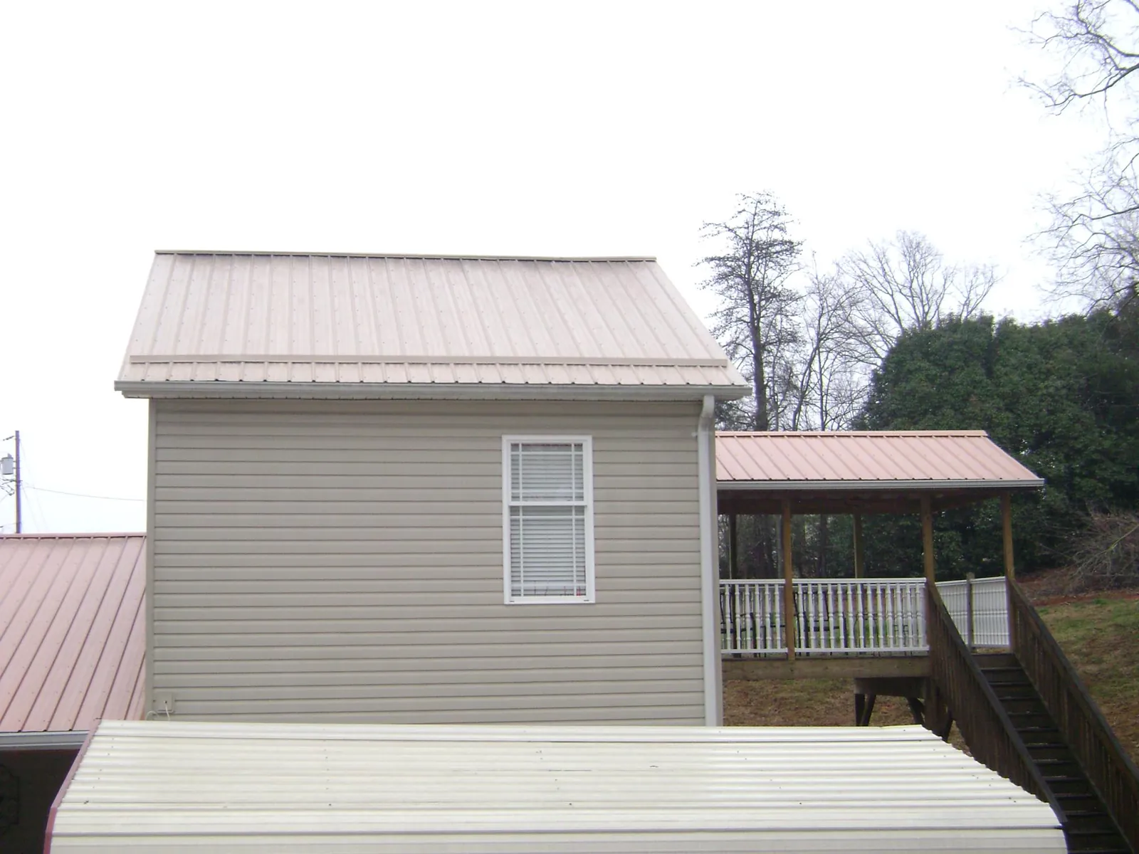 Tan metal roofs on a two story addition and attached porch, from a Roof Replacement job in North Vernon